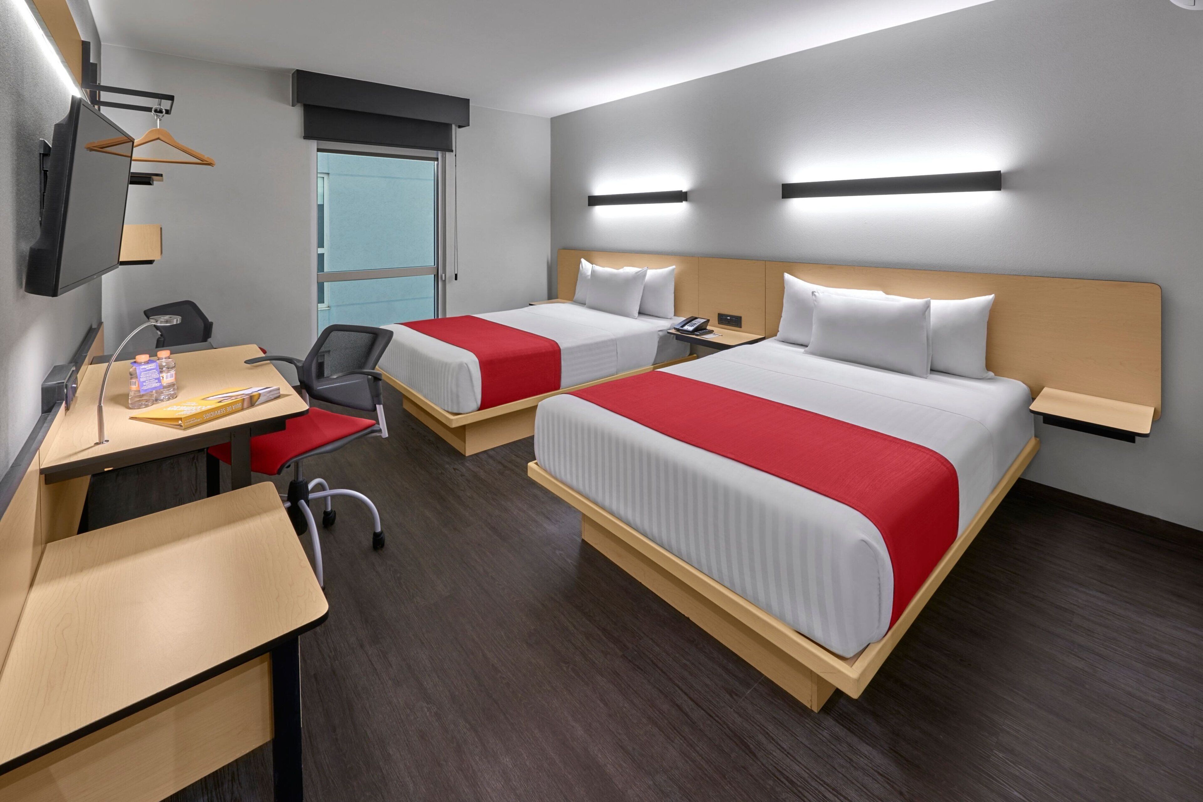 Une chambre d’hôtel avec deux lits, un bureau, une chaise, une télévision et une fenêtre.