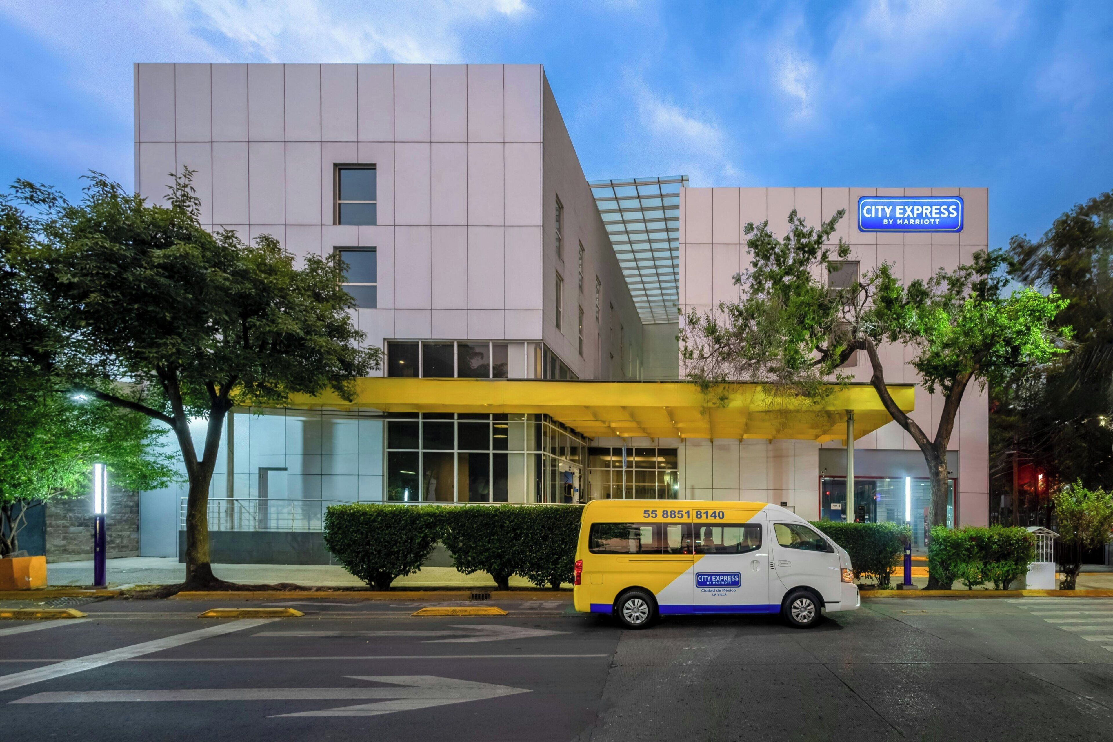 Een modern gebouw met een City Express by Marriott bord, een overdekte ingang en een geparkeerde City Express bestelwagen.