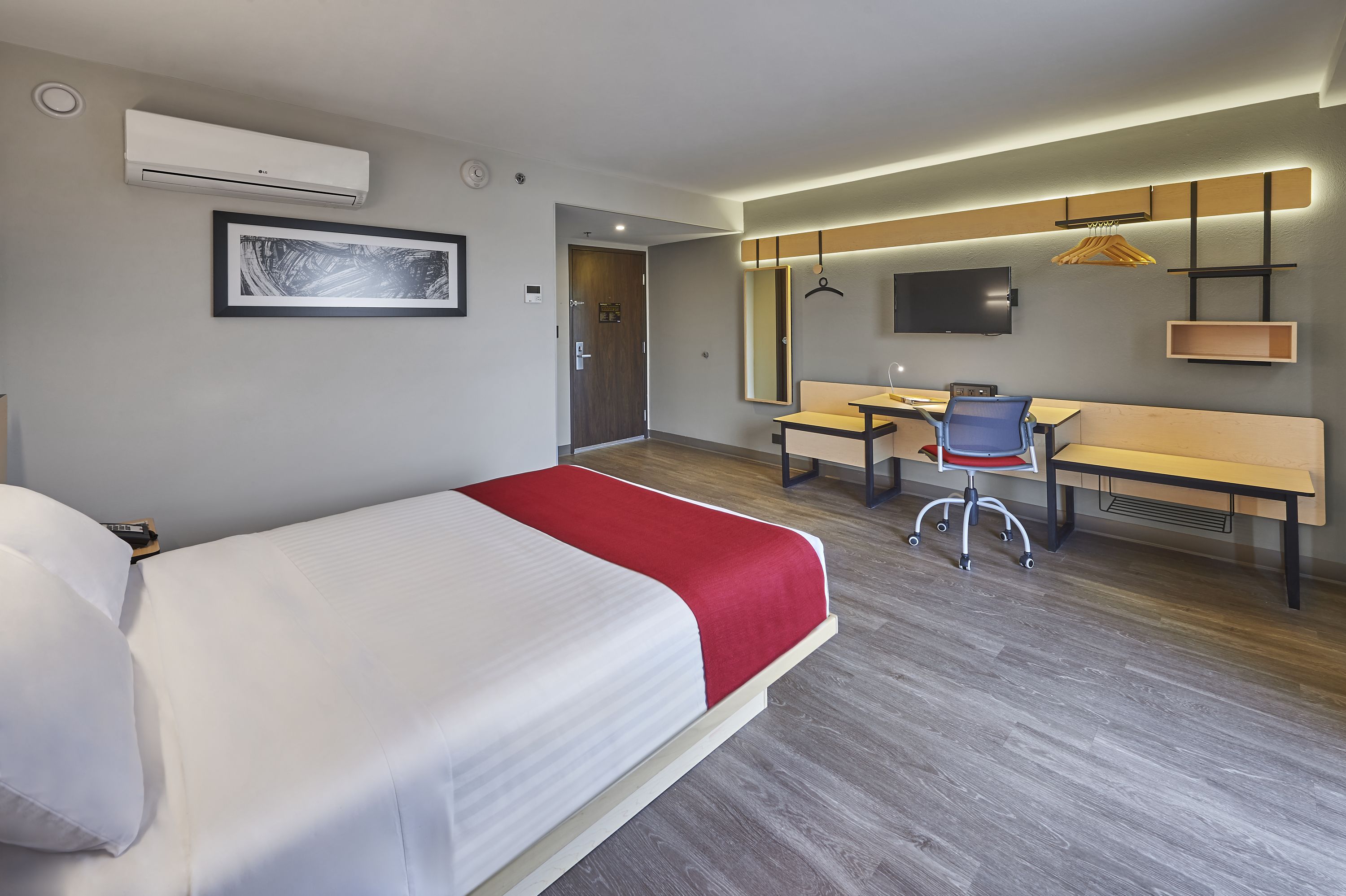 A modern hotel room with a bed, desk, chair, and a mounted TV.