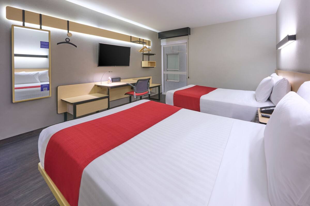 Een hotelkamer met twee bedden, een bureau, een stoel, een televisie en een raam.