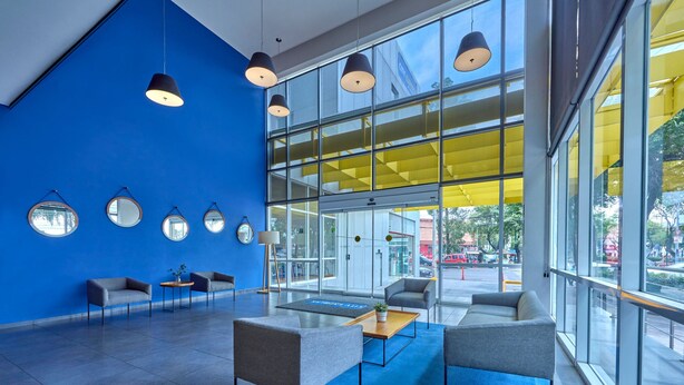 A modern lobby with blue walls, large windows, and a seating area with tables and chairs.