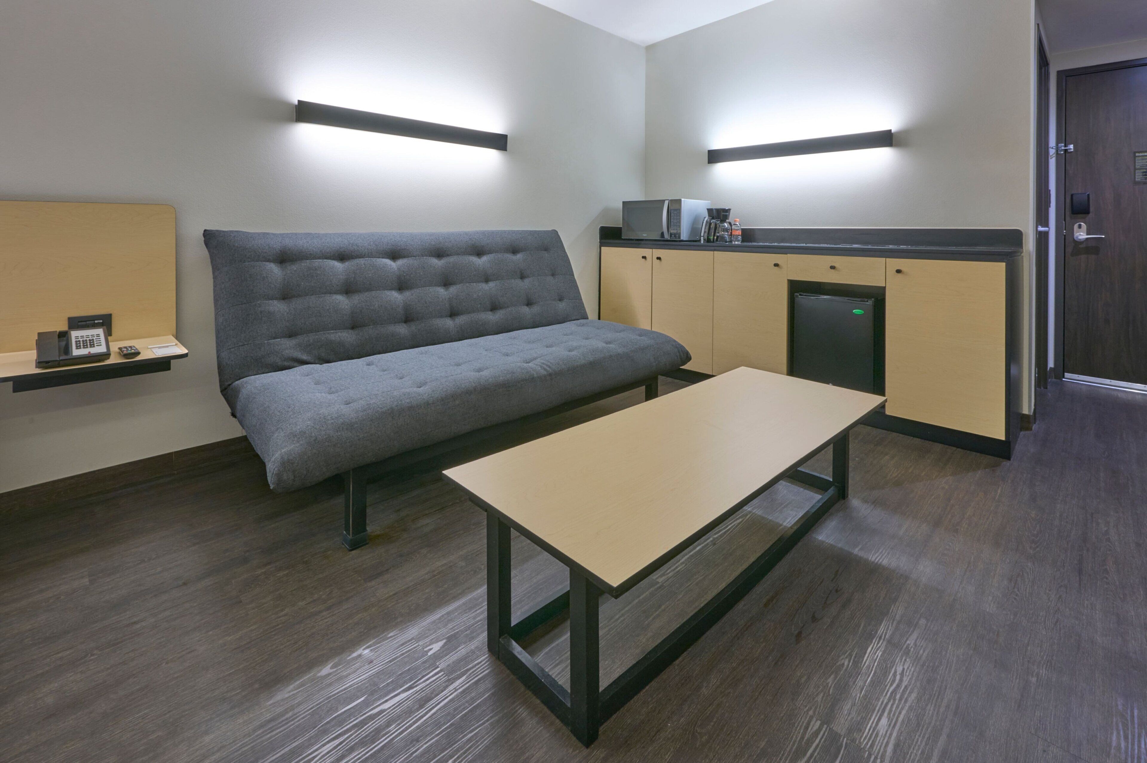 A modern room with a sofa, a table, a microwave, and a small cabinet.