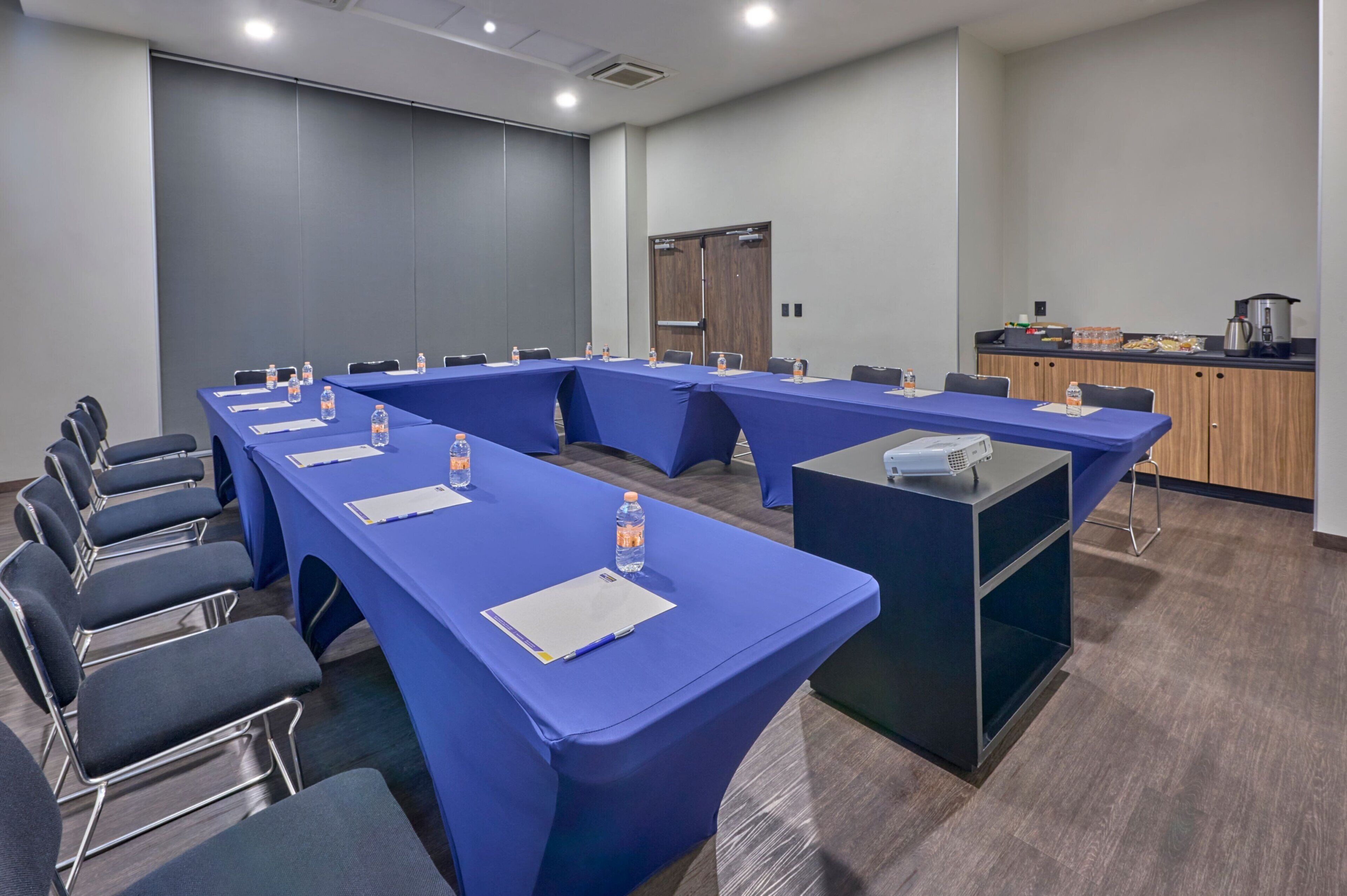 A conference room with long tables, chairs, and a kitchenette area.