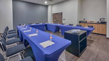 A conference room with long tables, chairs, and a kitchenette area.
