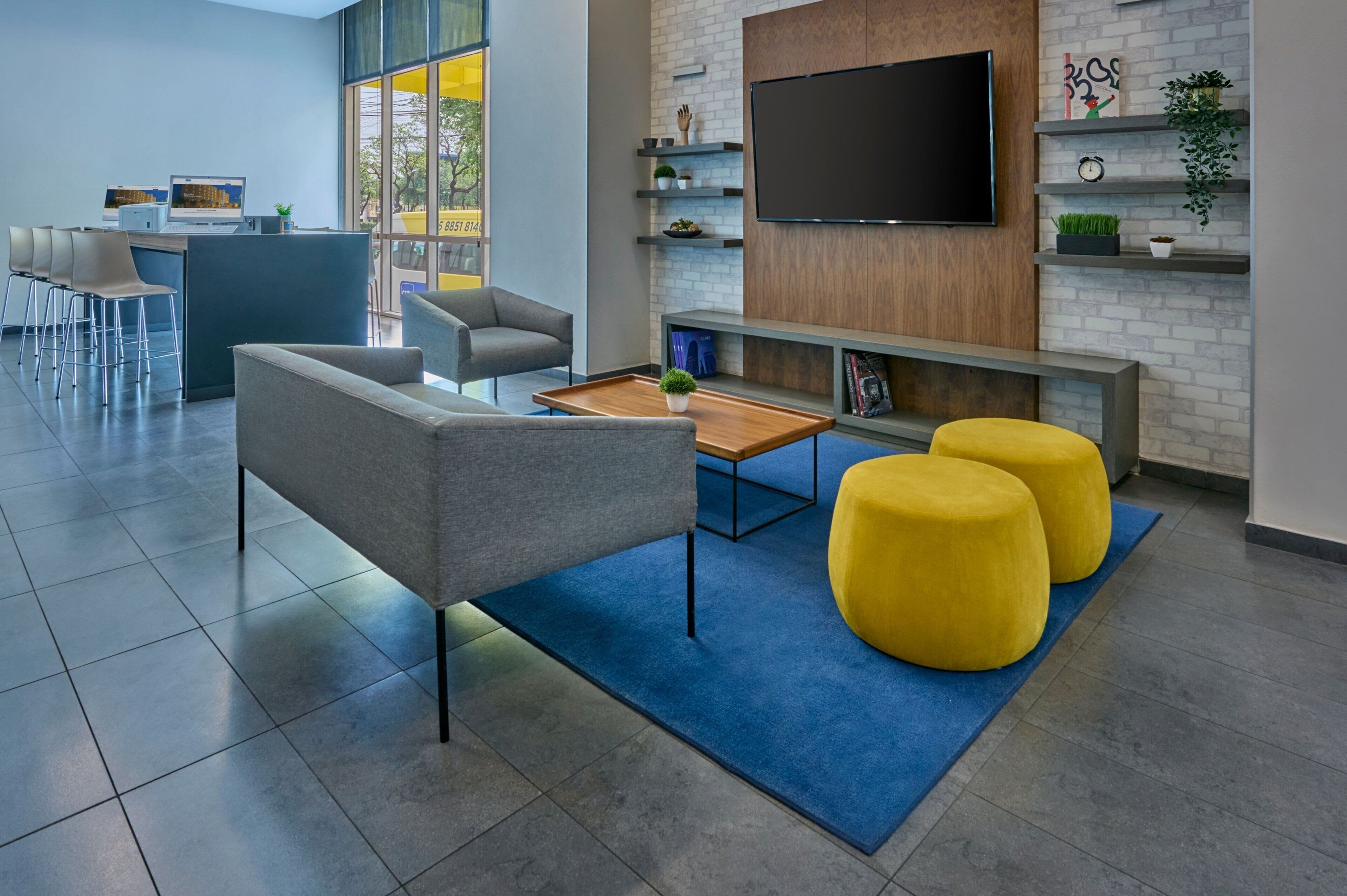 A modern office space with a reception area, seating, a large flat-screen TV, and a brick wall with shelves.