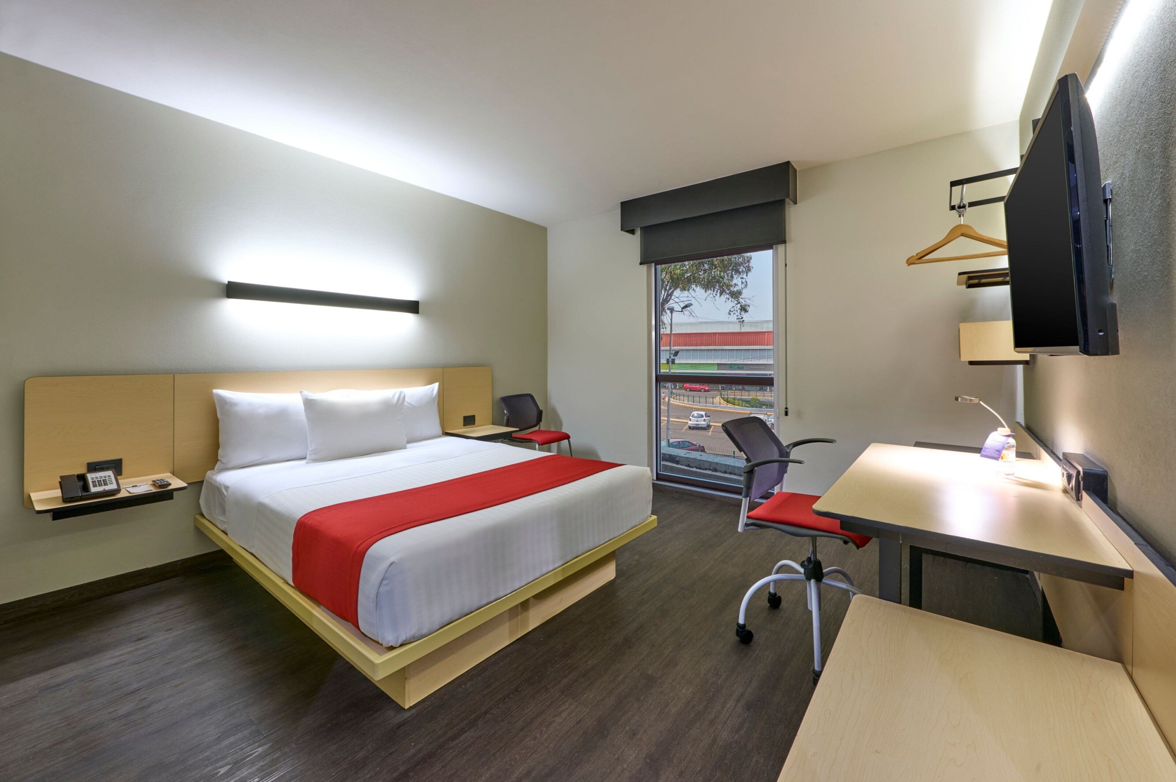 Habitación de hotel con cama, escritorio, silla y televisor montado en la pared.