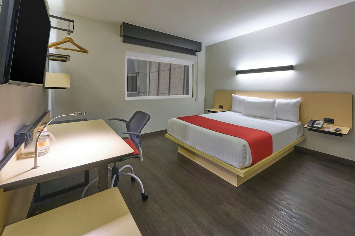 Een hotelkamer met een bed, bureau, stoel en een kleine tafel met een fles.