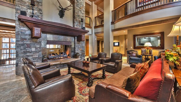 A spacious living area with a stone fireplace, leather furniture, and a high ceiling with wooden beams. - Miners Club by Canyons Village Rentals (Park City)
