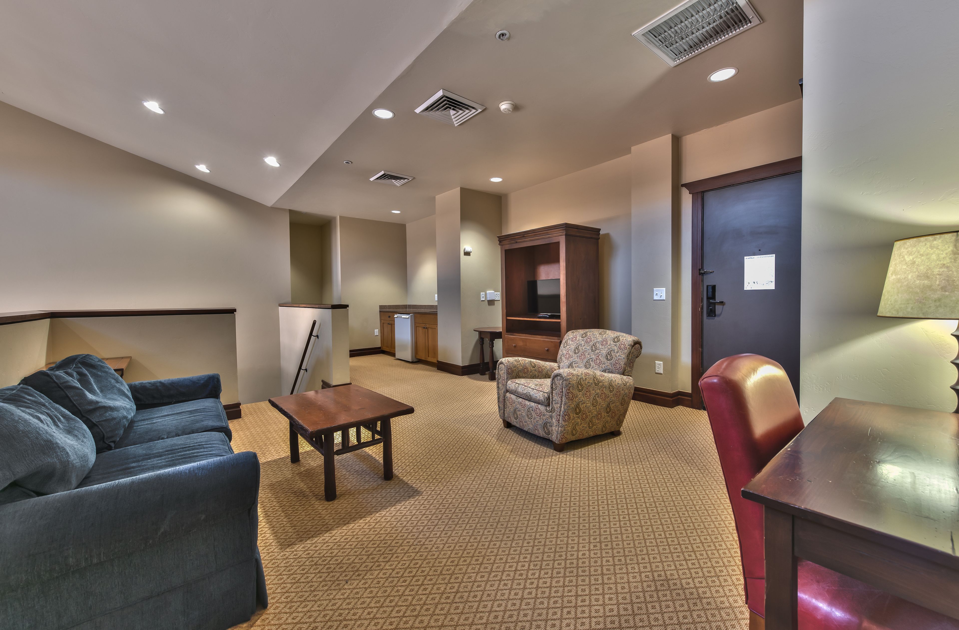 A hotel room with a sofa, armchair, and a small table. There is a cabinet and a door in the background.