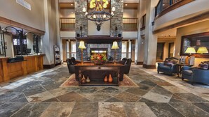 A spacious lobby with a central wooden reception desk, a stone fireplace, and a chandelier. - Miners Club by Canyons Village Rentals (Park City)