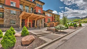 A multi-story hotel with a stone facade, a covered entrance, and a landscaped front yard with shrubs and rocks. - Miners Club by Canyons Village Rentals (Park City)