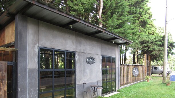 A building with large windows, a sign reading "TAYUA", and a fenced area with a truck parked nearby. - Ataco Luxury Cabin (Concepcion de Ataco)