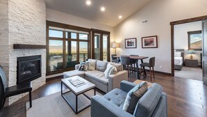 A spacious living room with a fireplace, comfortable seating, a dining area, and large windows offering a view of the landscape.