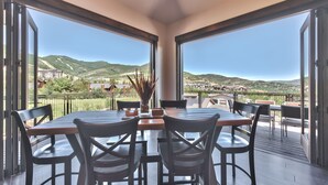 A dining area with a table and chairs, large windows with a view of a hilly landscape and buildings.