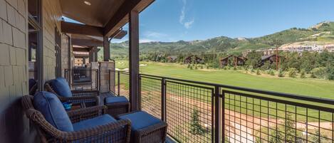 Un balcón con mobiliario de mimbre y vistas a un campo de golf y montañas.