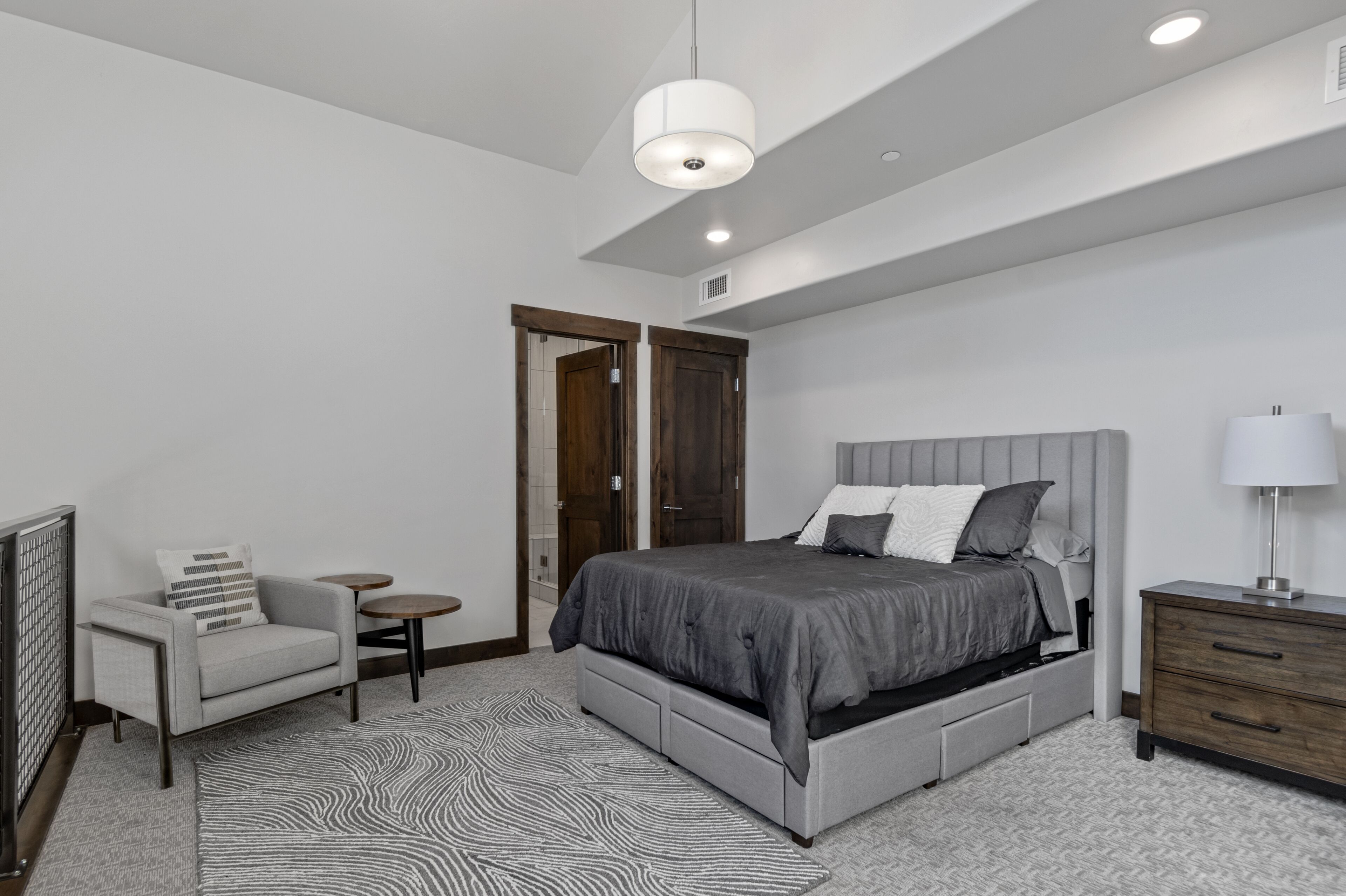 A modern bedroom with a large bed, a chair, a small table, and a nightstand.