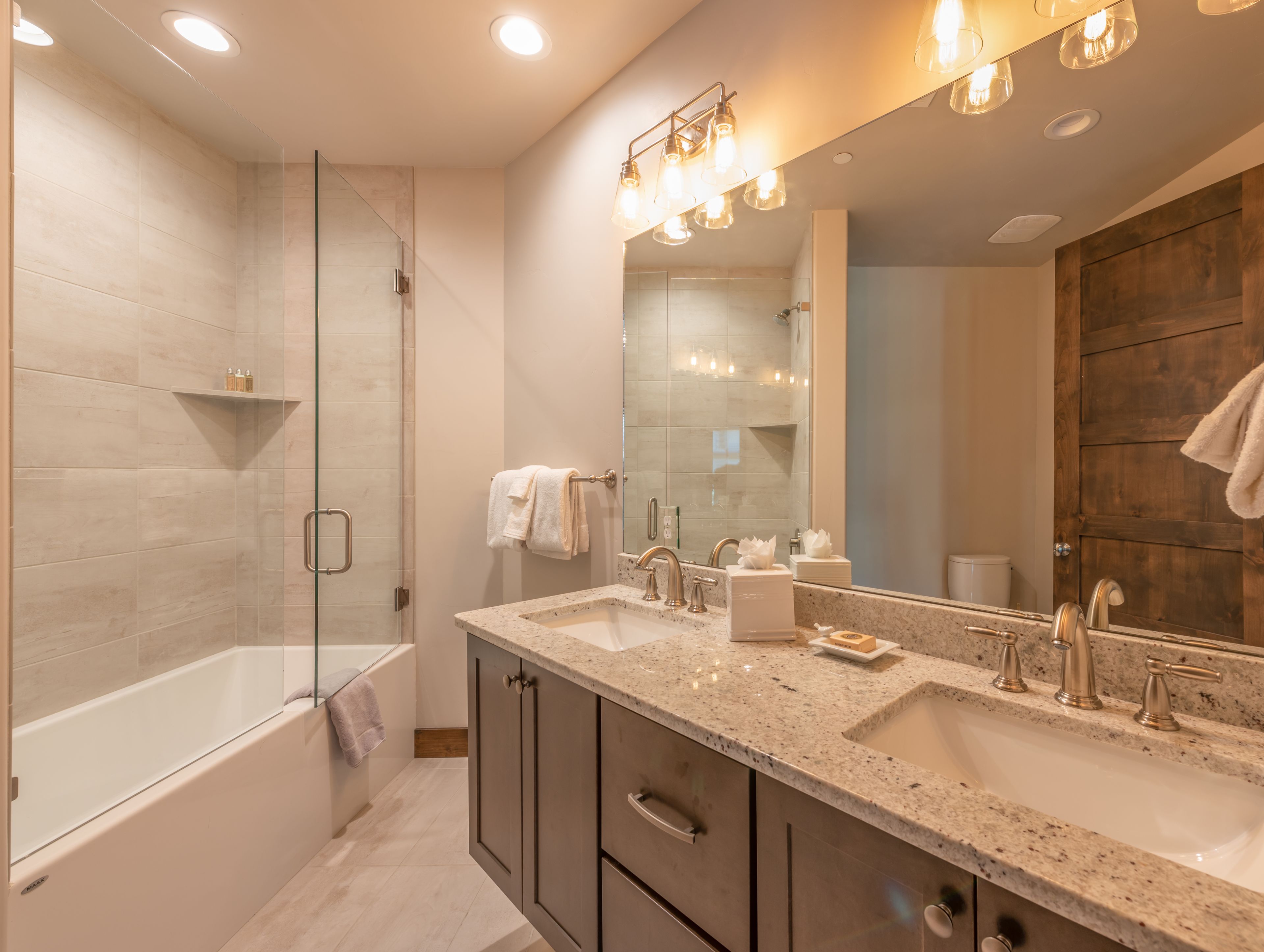 A modern bathroom with a large mirror, two sinks, a bathtub, and a shower.