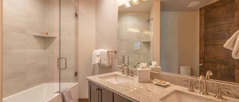 A modern bathroom with a large mirror, two sinks, a bathtub, and a shower.