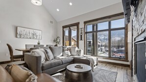 A spacious living room with a large sectional sofa, a round coffee table, and a view of a snowy landscape through large windows.