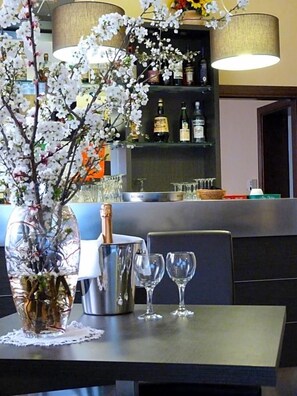 A bar area with a vase of flowers, a bottle of champagne, and glasses on a table.