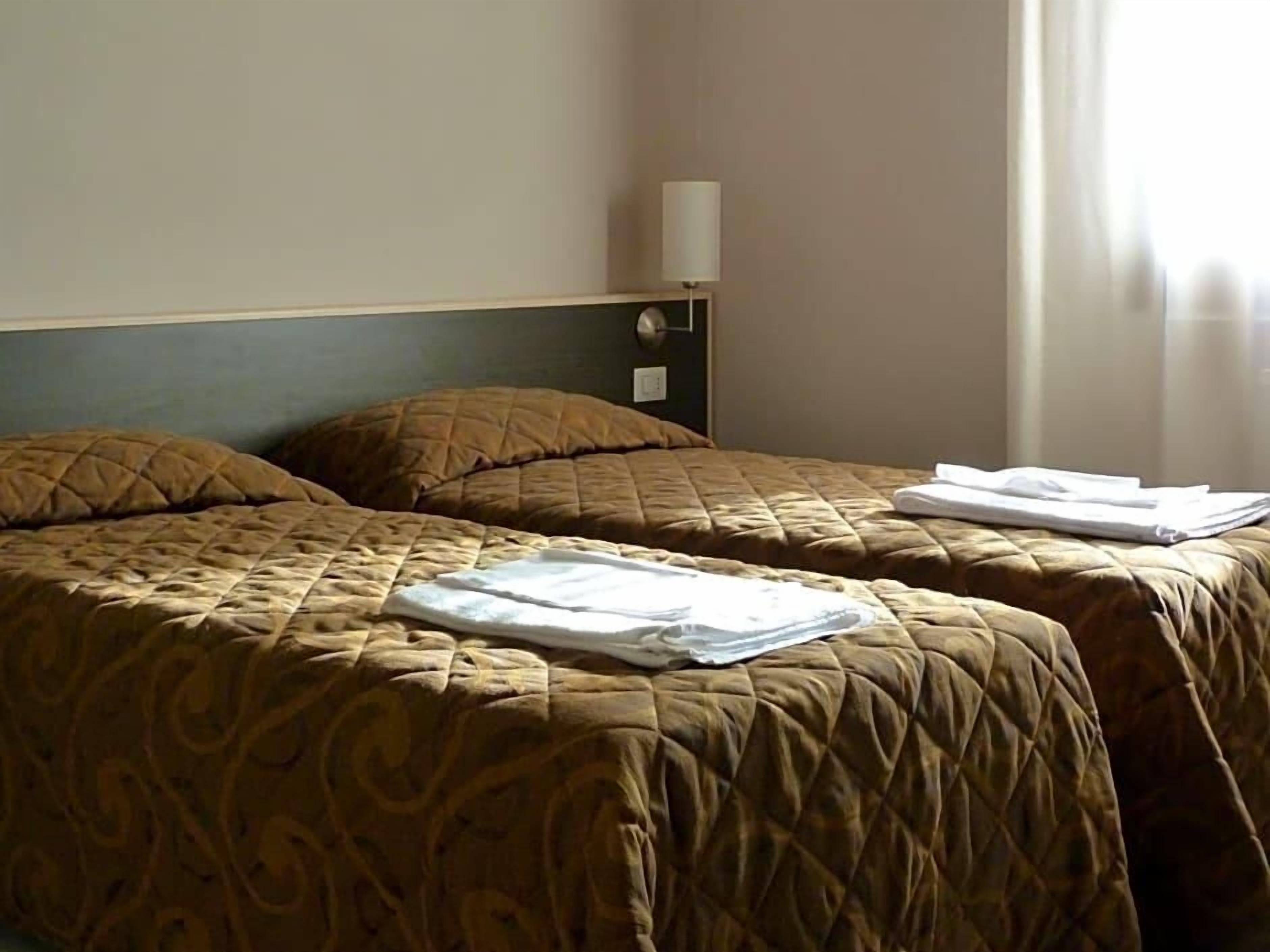 Een hotelkamer met twee bedden, een nachtkastje, een lamp en een raam met gordijnen.