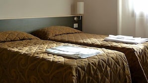 A hotel room with two beds, a nightstand, a lamp, and a window with curtains.