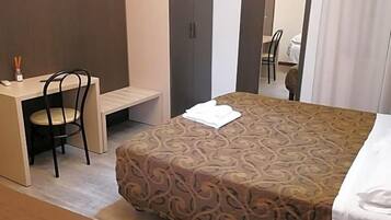 A hotel room with a bed, a desk with a chair, a television mounted on the wall, and a mirror.