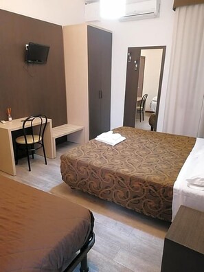 Una habitación de hotel con cama, escritorio con silla, televisor montado en la pared y espejo.