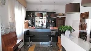 A hotel lobby with a reception desk, a bar area, a seating area with a bench, and a clock on the wall.