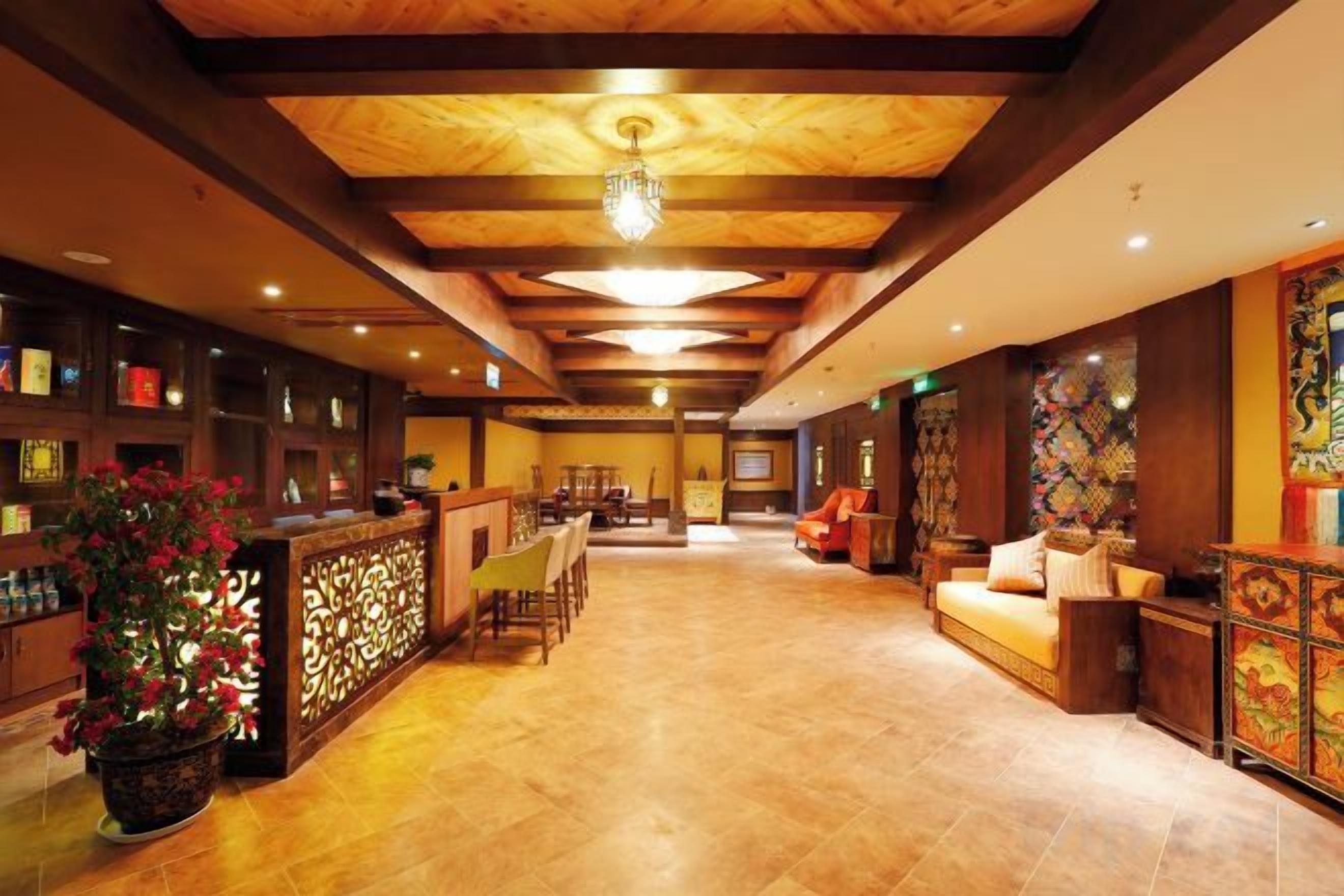 Um hall de hotel com teto de madeira, balcão de recepção, área de estar e painéis decorativos na parede.