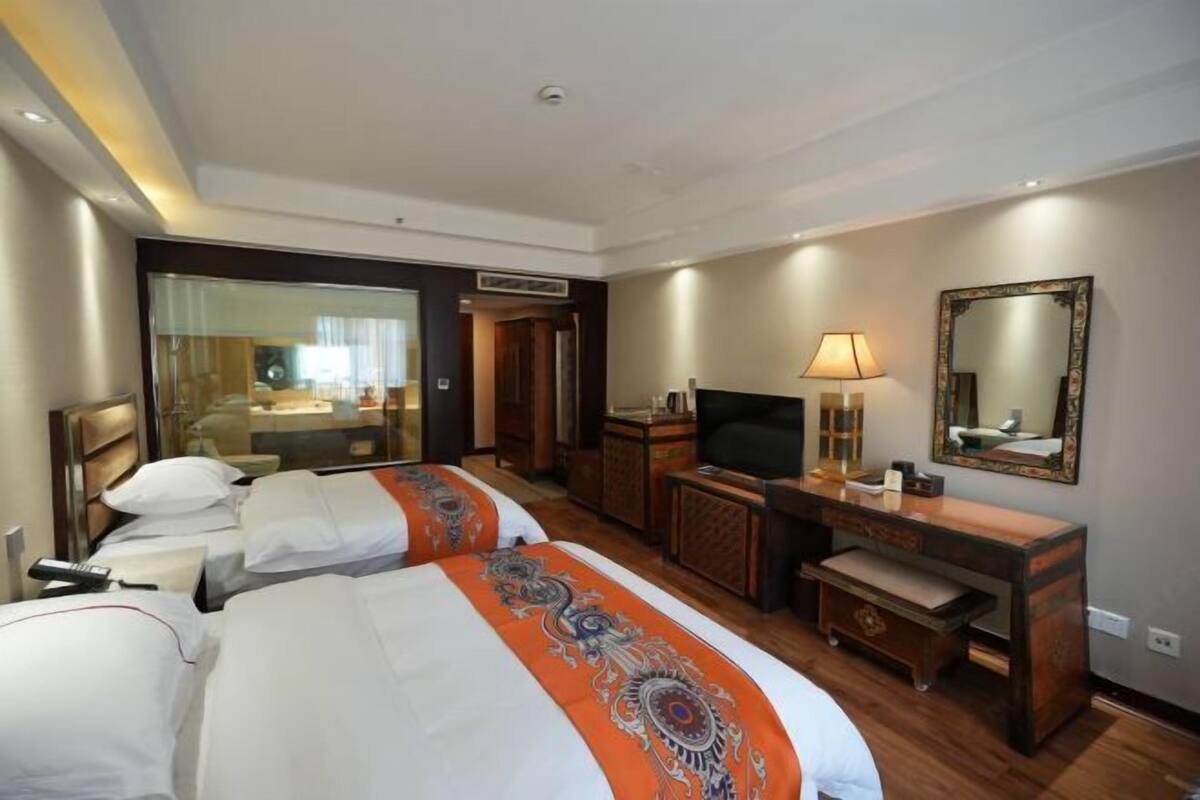 Een hotelkamer met twee bedden, een bureau, een televisie, een spiegel en een zichtbare badkamer door een glazen deur.