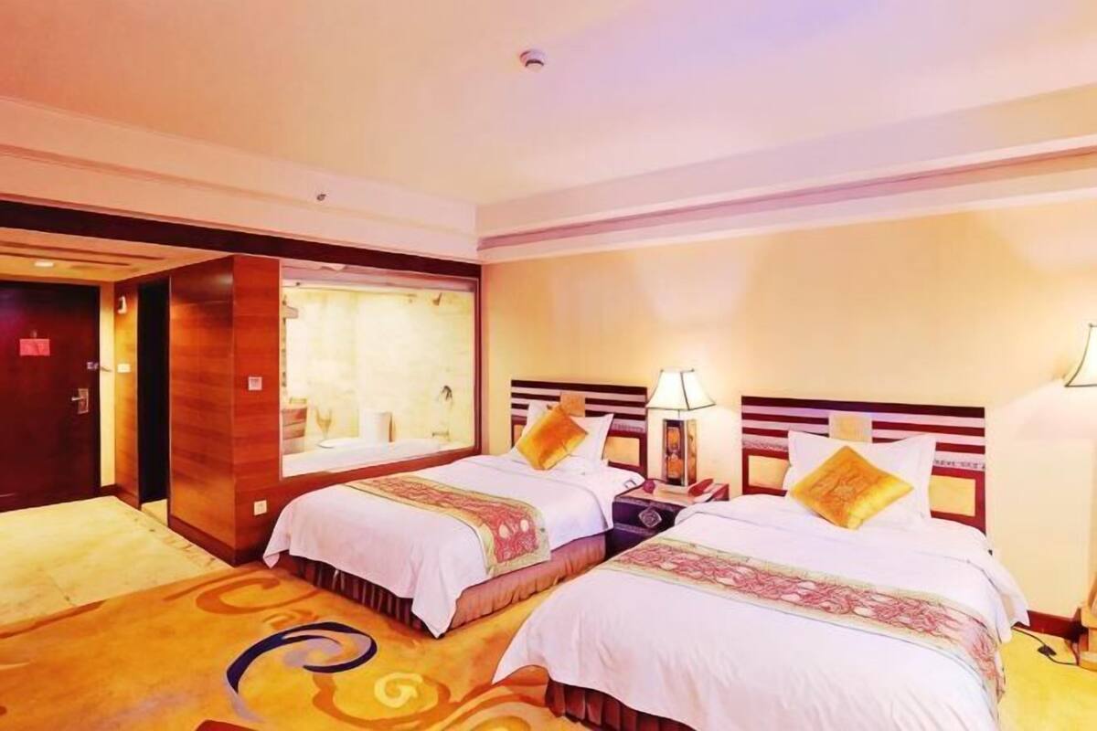 Een hotelkamer met twee bedden, een nachtkastje, een lamp en een raam met gordijnen.