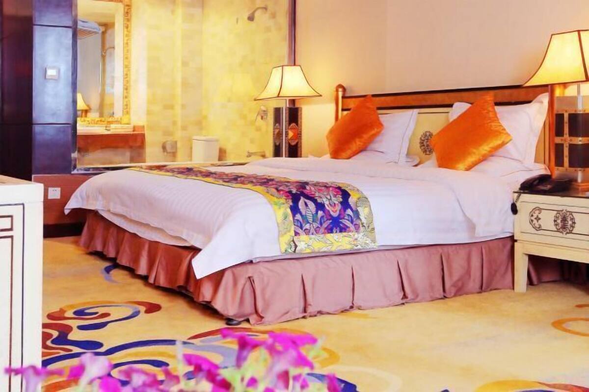 Een hotelkamer met een bed, twee bedlampen, een nachtkastje, een spiegel en een kamerbreed tapijt met dessin.