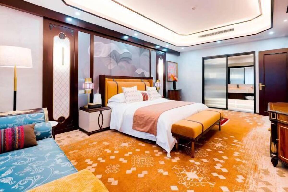 Een hotelkamer met een bed, nachtkastjes, een bank en een groot raam.