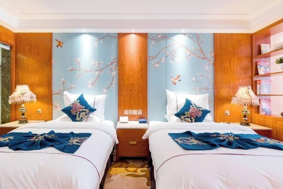 Een hotelkamer met twee bedden, houten lambrisering, bloemrijke wanddecoratie en bedlampen.