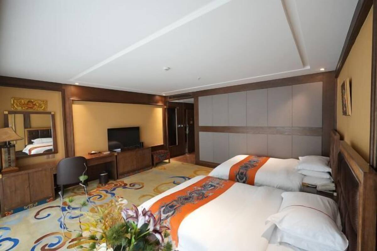 Een hotelkamer met twee bedden, een bureau, een stoel, een televisie en een decoratieve vaas.