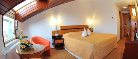 A hotel room with a large bed, a desk, a chair, and a window.