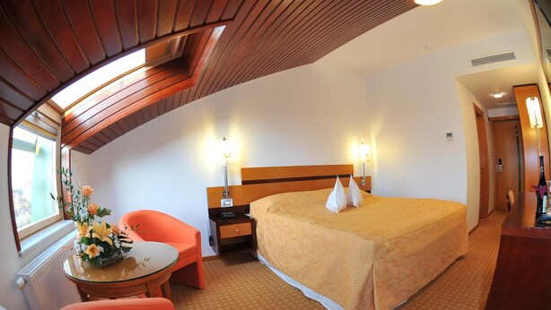 A hotel room with a large bed, a desk, a chair, and a window.