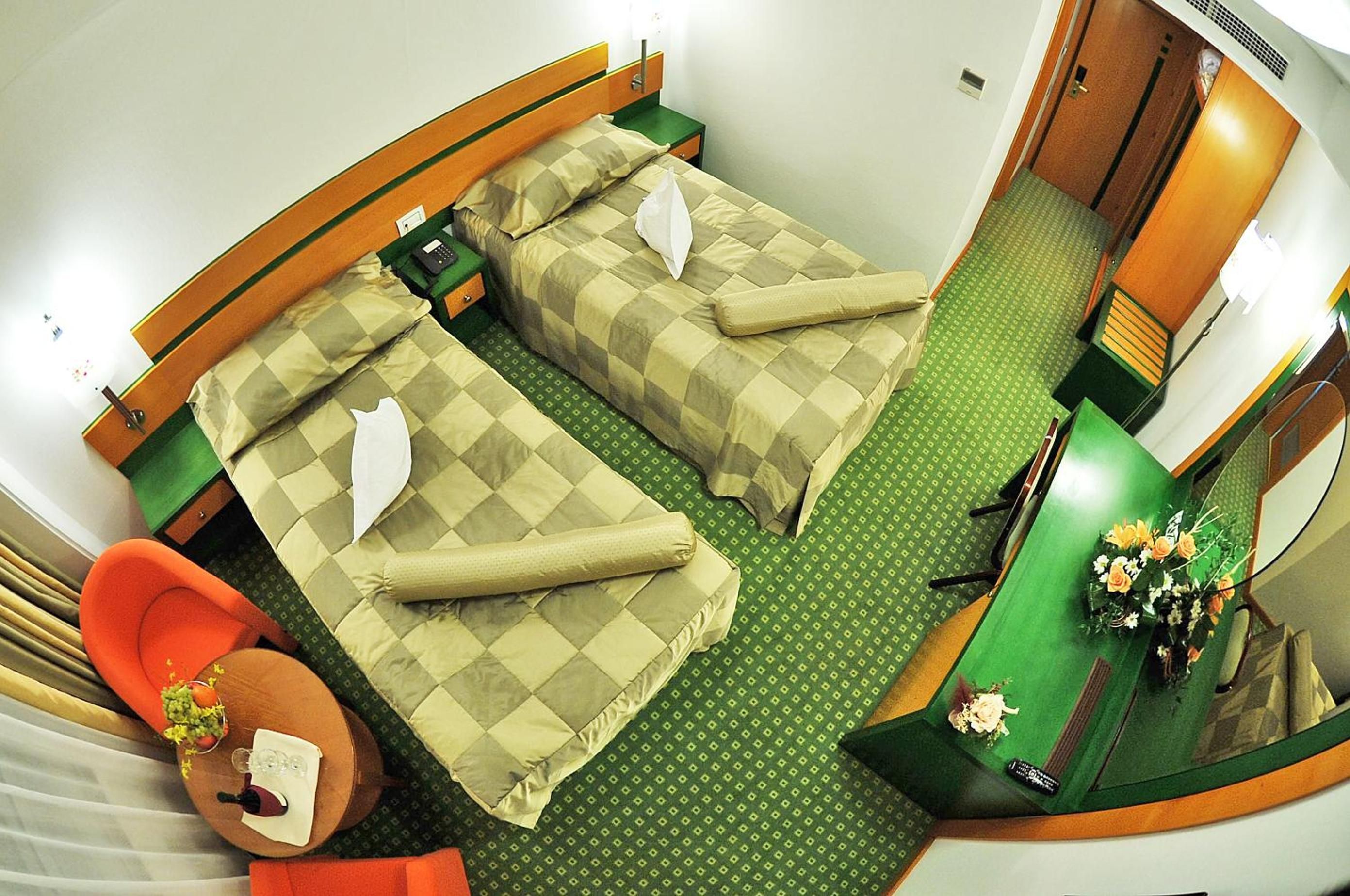 A compact hotel room with two beds, a small desk, a chair, and a bathroom.