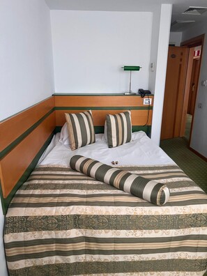 Una habitación de hotel con cama, almohadas, una mesita de noche con lámpara y teléfono.