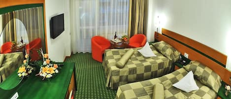 Una habitación de hotel con dos camas, un escritorio con silla, televisor y ventana con cortinas.