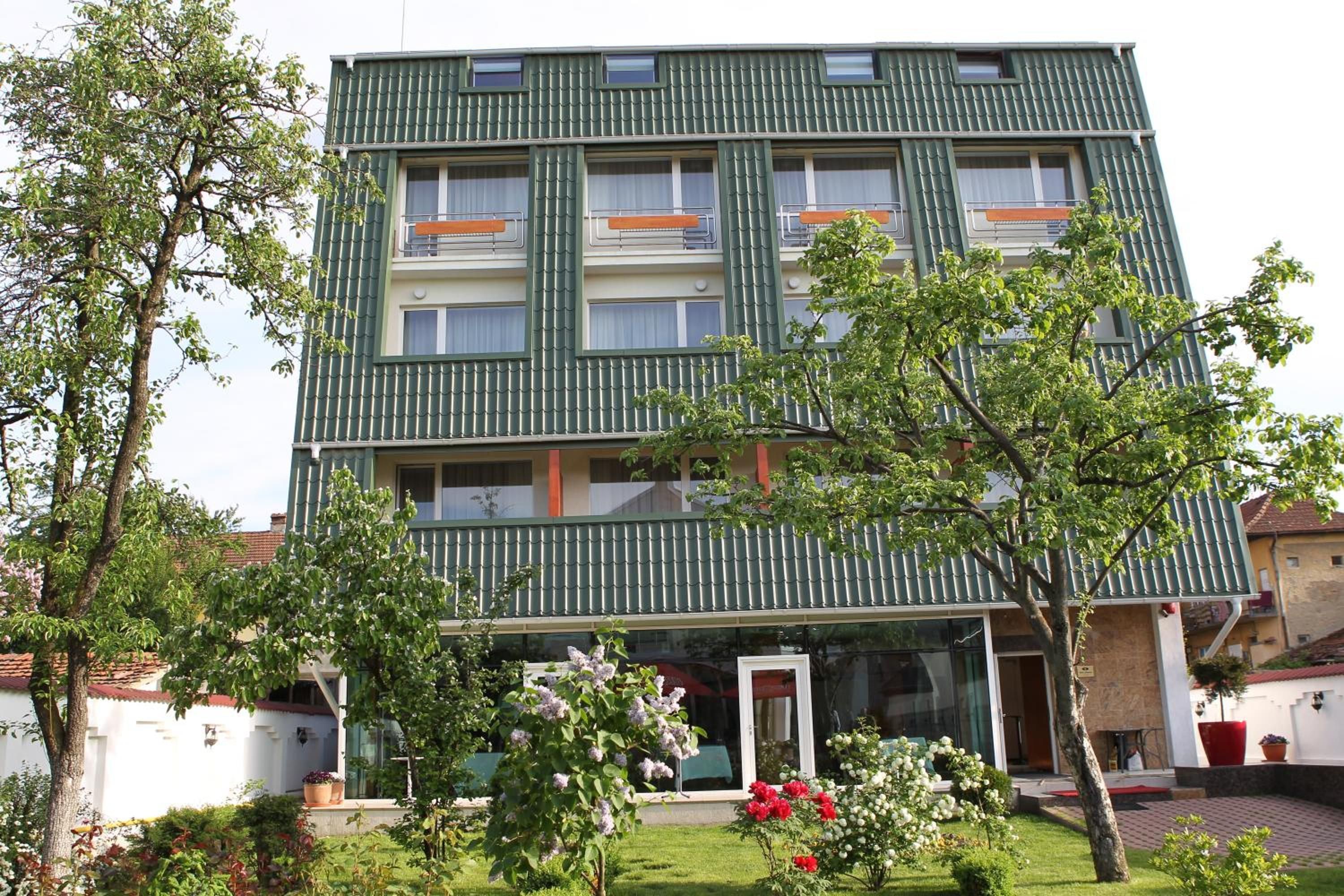Een meerhoog gebouw met balkons, een tuin vol bloemen en een heldere lucht.