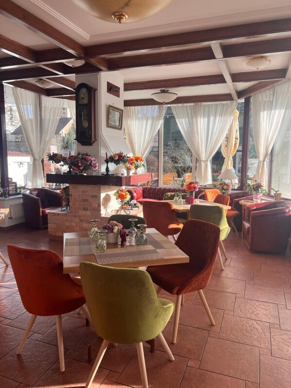 A dining area with a brick fireplace, wooden beams, and large windows with curtains.