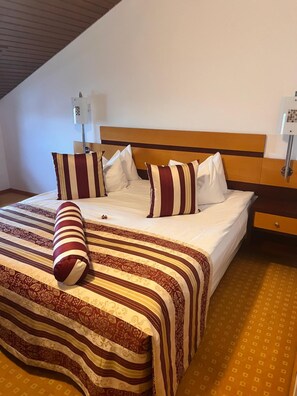Une chambre d’hôtel avec un lit, des oreillers, une table de chevet et une lampe.