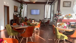 A restaurant with wooden tables and chairs, a television screen, and decorative plants.