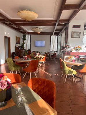 Un restaurant avec des tables et des chaises en bois, un écran de télévision et des plantes décoratives.