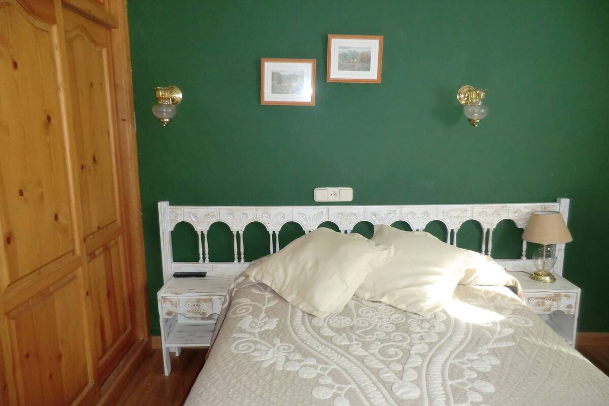 Un dormitorio con una cama, una mesita de noche, una lámpara y dos marcos de cuadros en la pared.