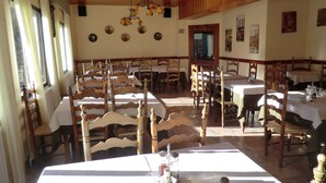 A dining area with wooden chairs and tables, a chandelier, and wall decorations. - Pensión Malida (Vielha e Mijaran)