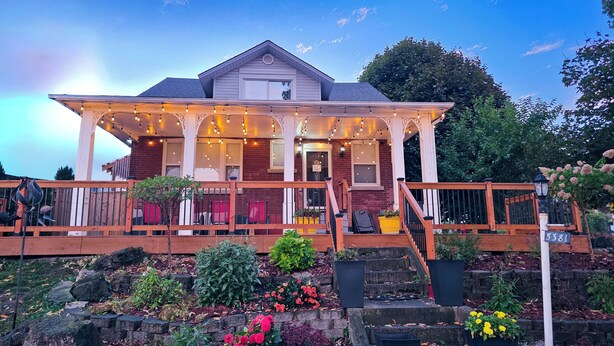 A two-story house with a porch, a staircase, and a garden with various plants and flowers. - Serene Niagara Inn (Niagara Falls)