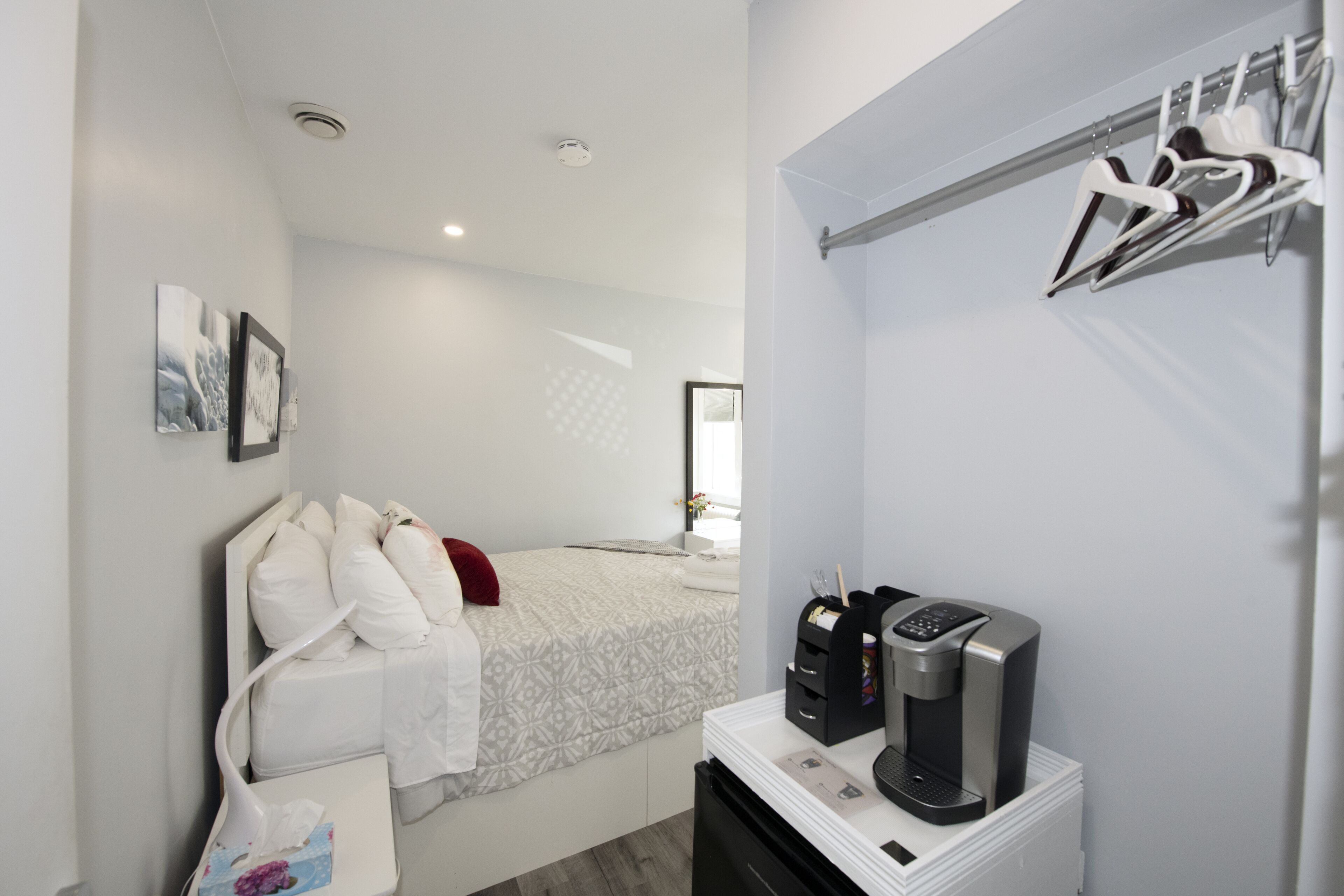 Une chambre d’hôtel moderne avec un lit bien fait, une machine à café et un porte-manteau fixé au mur.